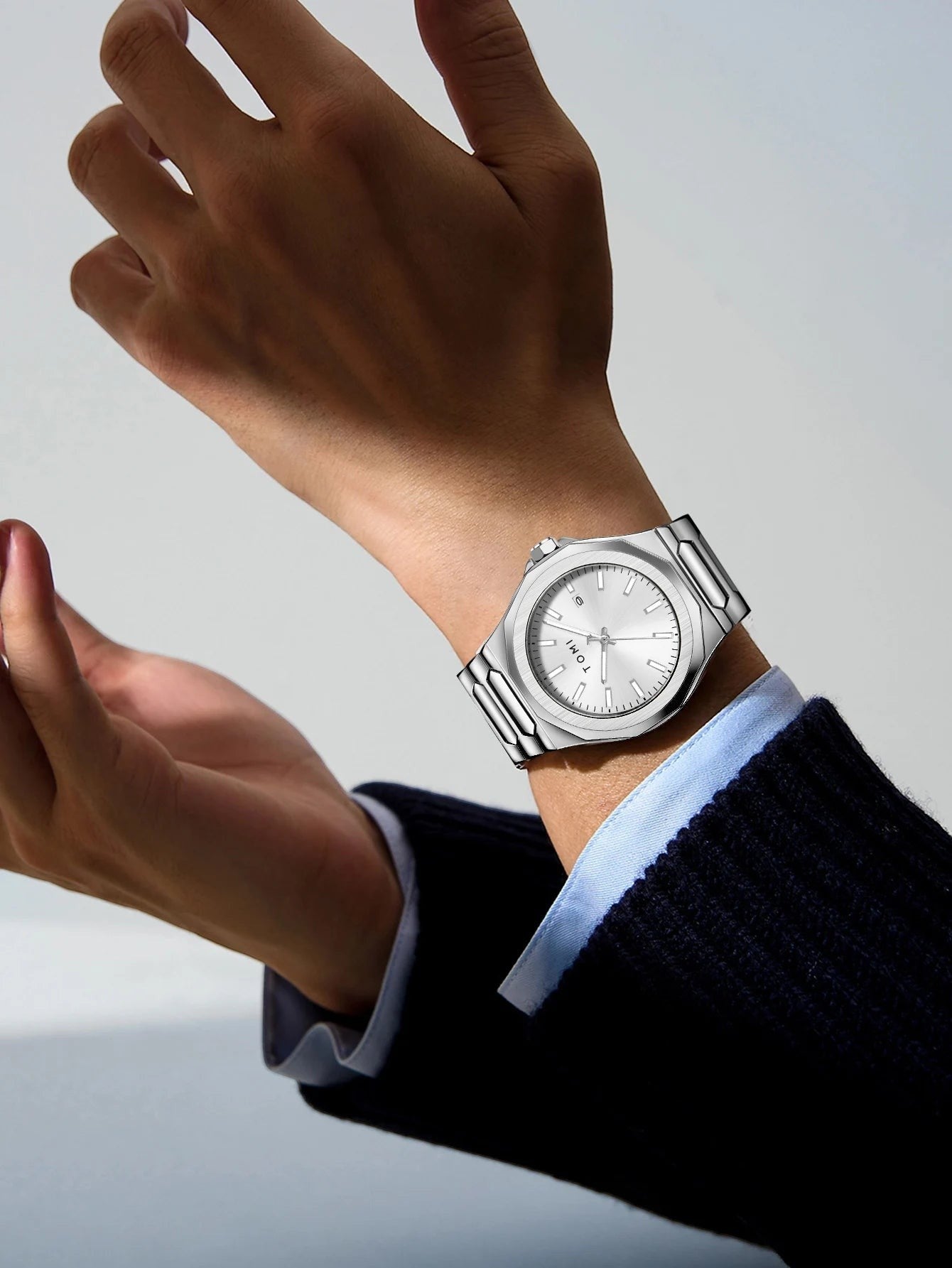 My Store TOMI luxury silver stainless steel wristwatch worn on a man's wrist with a navy blue sweater sleeve.